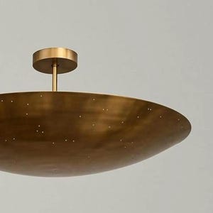 Puede incluir: Una l&aacute;mpara de techo empotrada de color lat&oacute;n. La l&aacute;mpara tiene una base circular y una pantalla grande, poco profunda, en forma de cuenco con peque&ntilde;as perforaciones espaciadas uniformemente. La luz est&aacute; montada en un v&aacute;stago corto.