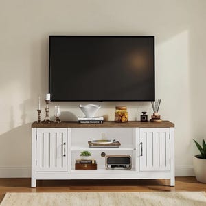 May include: A white television stand with a dark wood-toned top surface, featuring two side cabinets with vertical paneling and black handles, and an open center shelf containing a record player, a small potted plant, and a vintage-style radio.