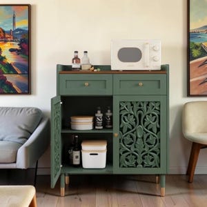 May include: A sage green wooden cabinet with two drawers and a lower storage area featuring one open shelf and one door with intricate floral carvings. The cabinet has a brown top surface, gold-toned knobs, and light-colored legs with gold tips.