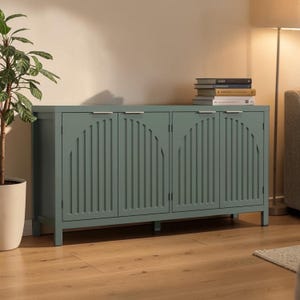 May include: A teal-colored wooden cabinet with four doors and silver handles. The doors feature a vertical, arched design. The cabinet is placed against a neutral wall, with a plant and books visible in the background.
