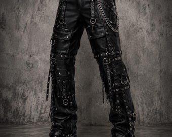 May include: Black faux leather cargo pants featuring multiple silver-toned metal rings, chains, and studs. The pants include several cargo pockets, adjustable straps with buckles, and a button closure at the waist, paired with black leather boots.