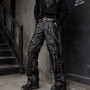 May include: A black long-sleeved shirt with a graphic print and silver cross necklaces paired with black cargo pants featuring multiple pockets, metal D-rings, silver chains, and buckled straps, worn with chunky black platform boots and a studded belt.