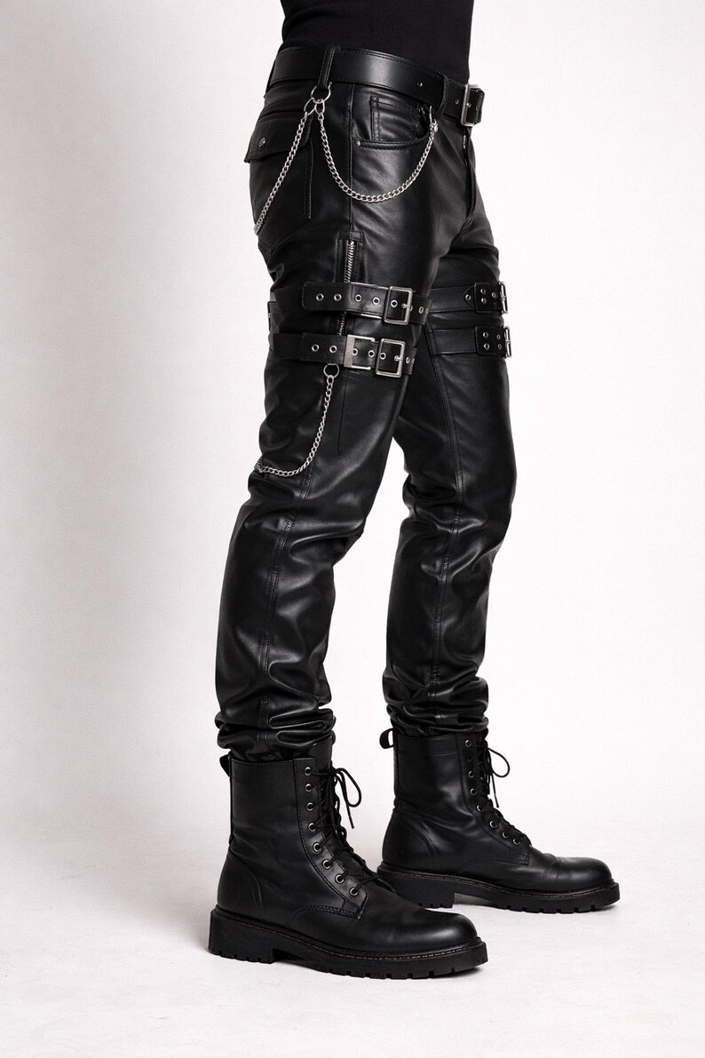 May include: Black leather pants with multiple silver buckles and chains. The pants have a fitted design with a belt and pockets. The model is wearing black combat boots. The overall style is edgy and alternative.