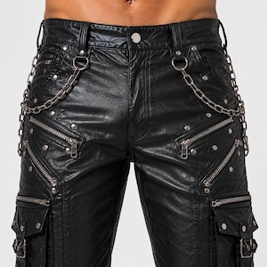 Puede incluir: Pantalones negros con acabado texturizado, múltiples cremalleras de metal plateado y tachuelas decorativas. Los pantalones incluyen dos grandes bolsillos cargo con cierres de hebilla y dos cadenas de metal plateado en las trabillas.