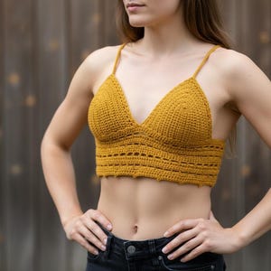 Peut inclure: Haut en crochet jaune moutarde avec fines bretelles et un col en V. Le haut présente un motif texturé et une bande ajourée décorative en bas. Le vêtement est fait à la main et convient aux climats chauds.