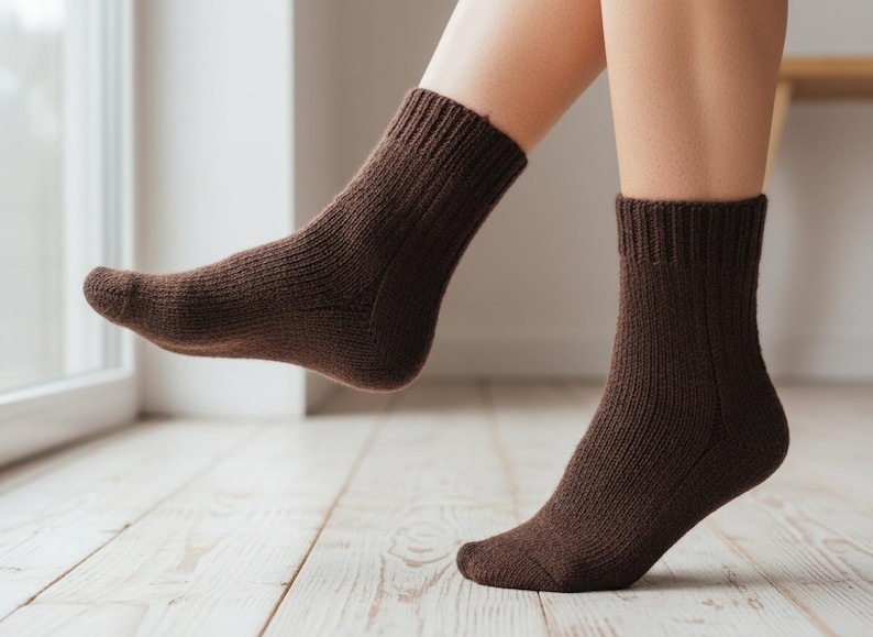 Pu&ograve; includere: Un paio di calzini marroni a maglia a coste. I calzini sono indossati sui piedi di una persona, con un piede leggermente sollevato da un pavimento in legno chiaro. I calzini hanno un aspetto spesso e strutturato.