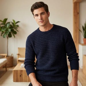 Può includere: Un maglione blu navy girocollo con un motivo a maglia strutturato. Il maglione è indossato da una persona in una stanza ben illuminata con toni neutri e piante da interno. È uno stile classico.