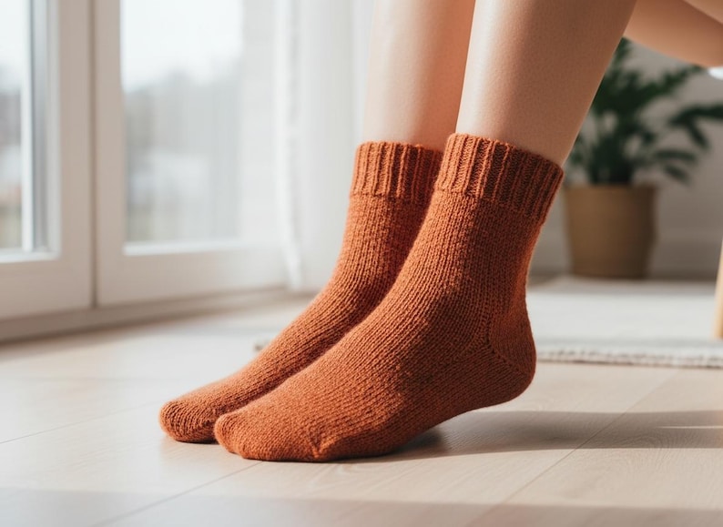 Pu&ograve; includere: Un paio di calzini lavorati a maglia color ruggine. I calzini hanno polsini a coste e un motivo a maglia strutturato. I calzini sono indossati all'interno, con una finestra e una pianta in vaso sullo sfondo. I calzini sembrano essere fatti di un materiale caldo e morbido.