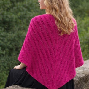 Peut inclure: Un poncho tricoté rose fuchsia vif avec un motif en chevrons. Le poncho est porté sur une robe noire, créant un contraste saisissant. Le vêtement est fait d'une matière douce et texturée, parfaite pour les temps frais.