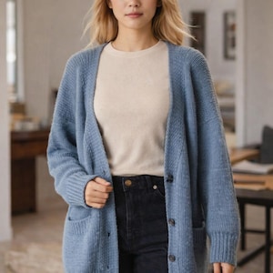 May include: A light blue cardigan with a textured knit design. The cardigan has a button-up front, two front pockets, and long sleeves. The person is wearing a cream-colored top and dark jeans.