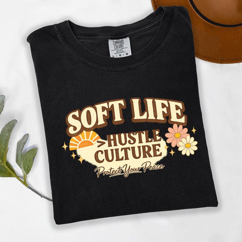 May include: Black t-shirt with the words "SOFT LIFE HUSTLE CULTURE Protect Your Peace" in a retro design. The graphic includes a sun, flowers, and stars. The shirt is a Comfort Colors brand.