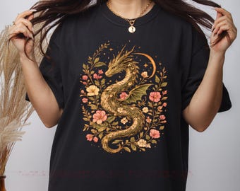 May include: A black t-shirt featuring a central graphic of a golden dragon coiled among various flowers and foliage. The design includes a crescent moon shape above the dragon, rendered in warm tones of gold, orange, and pink against the dark fabric.