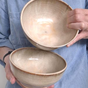 Op de afbeelding: Twee ronde keramische kommen met een gladde, glanzende afwerking. De kommen hebben een kleurverloop dat overgaat van een zacht, romig beige in het midden naar een warme, getoaste bruine kleur langs de afgeronde randen.