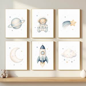 May include: Six framed art prints with watercolour illustrations of space-themed elements. The prints depict a planet, a teddy bear astronaut, a shooting star, a crescent moon, a rocket, and a cloud with stars. The frames have a gold finish.