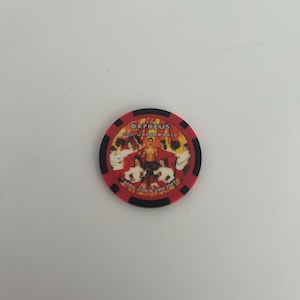 May include: A red and black casino chip with the text "Orpheus in the Underworld" and the dates "April 27th & 29th 2007". The chip features a central image of a muscular figure surrounded by other figures.