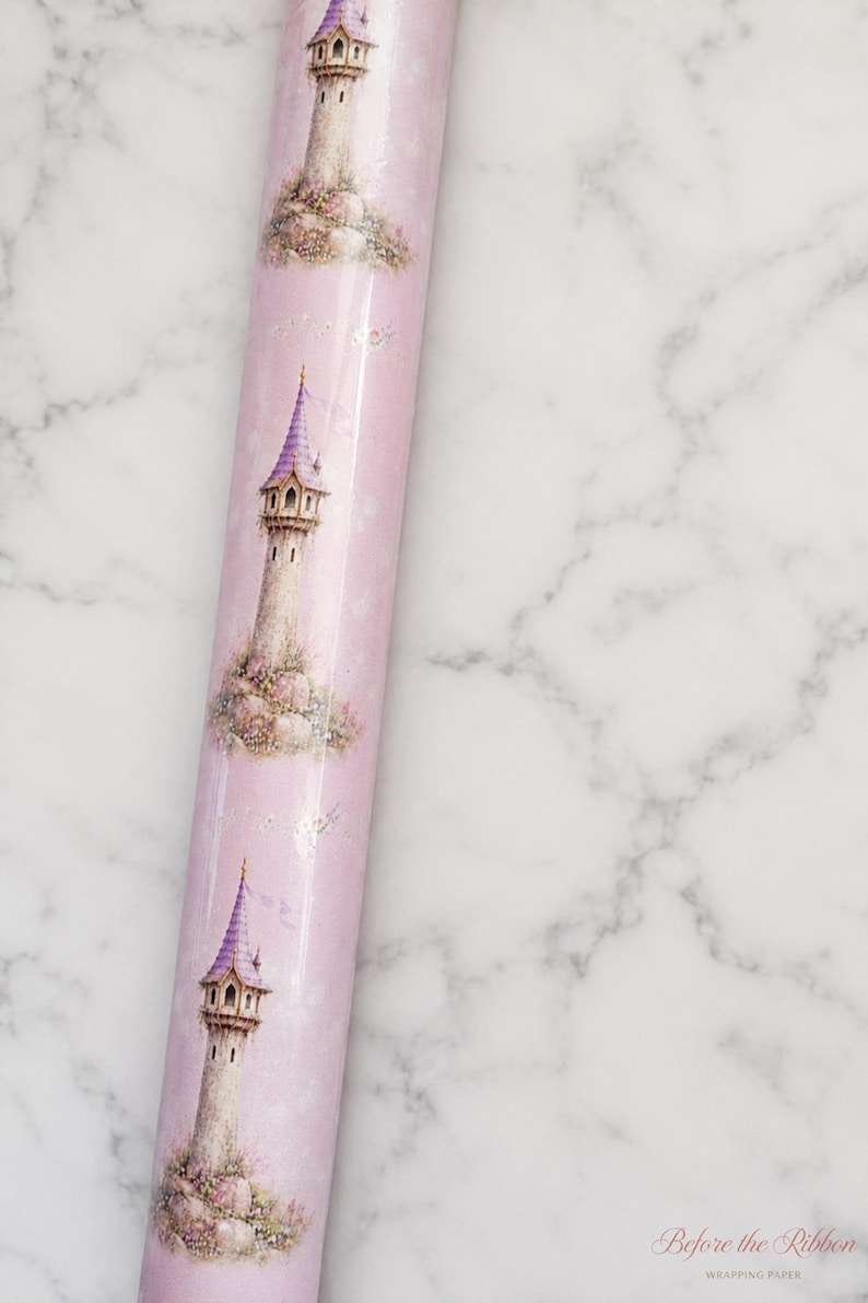 Puede incluir: Un rollo de papel de regalo rosa claro con un patr&oacute;n repetitivo de torres de piedra altas con techos c&oacute;nicos morados. Cada torre est&aacute; rodeada de peque&ntilde;as flores coloridas y vegetaci&oacute;n. El papel tiene un acabado liso y brillante.