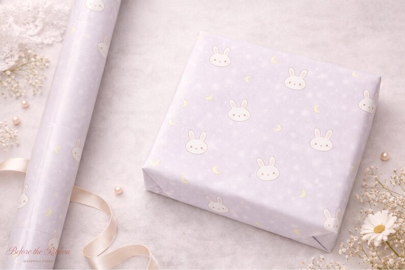 May include: A roll of wrapping paper and a wrapped gift box. Both are light purple with a repeating pattern of white bunny faces, stars, and crescent moons. The scene is decorated with pearls, flowers, and a ribbon.
