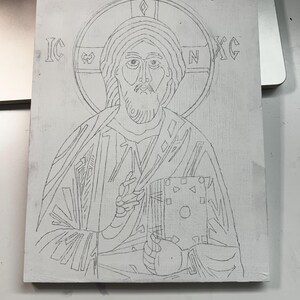 Pu&ograve; includere: Un pannello rettangolare bianco con un disegno a matita di grafite raffigurante una figura con un'aureola che tiene in mano un libro. Le lettere IC e XC sono visibili su entrambi i lati dell'aureola. Il disegno mostra una persona barbuta.