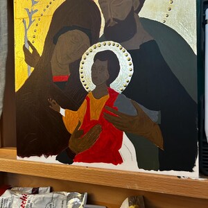 Pu&ograve; includere: Un dipinto religioso su pannello rettangolare che raffigura tre figure con aureole su sfondo dorato. Il bambino centrale indossa una tunica rosso brillante, affiancato da due adulti in abiti scuri. Il bambino tiene in mano un uccellino grigio.