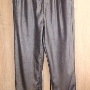 Peut inclure: Pantalon gris métallisé suspendu à un cintre noir. Le pantalon a une coupe droite avec un léger éclat. Le pantalon est fait d'un tissu lisse et comporte une fermeture à bouton et à glissière. Le pantalon est suspendu devant une armoire en bois brun clair.