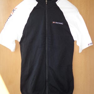 May include: Black and white zip-up athletic top. The short sleeves are white, and the body is black with a full-length zip. The brand name "X BIONIC" is printed on the chest. The top is hanging on a hanger.