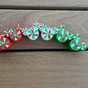 May include: A set of decorative hooks featuring circular peppermint candy designs in red, white, and green. Each hook is shaped like a mouse head with smaller circular accents, and includes a silver-toned metal hook attached to the front.