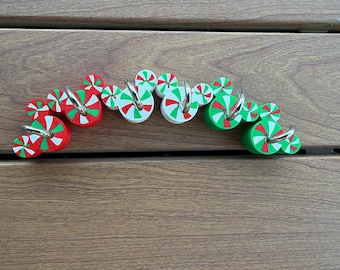 May include: A set of decorative hooks featuring circular peppermint candy designs in red, white, and green. Each hook is shaped like a mouse head with smaller circular accents, and includes a silver-toned metal hook attached to the front.