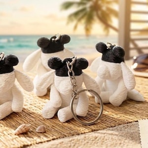 May include: Four small plush sheep keychains with white bodies and black heads, each featuring floppy ears and a metal ring attachment. The keychains are arranged together, and a small card in the corner displays the text Evie KeyChain.