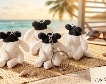 May include: Four small plush sheep keychains with white bodies and black heads, each featuring floppy ears and a metal ring attachment. The keychains are arranged together, and a small card in the corner displays the text Evie KeyChain.
