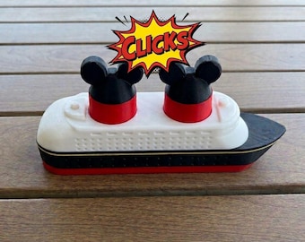 May include: A white, black, and red toy ship featuring two smokestacks topped with black mouse ears. Above the ship, a yellow and red comic-style speech bubble contains the word CLICKS in bold black letters. The ship has a white deck.