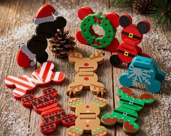 May include: A collection of nine holiday-themed plastic clips featuring various designs including a Santa hat, a green wreath, a red suit with a belt, a candy cane stripe, a reindeer, a snowflake, a red and black pattern, a gingerbread man, and an elf suit.