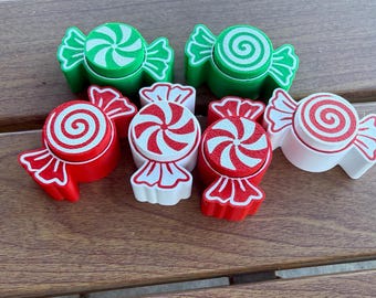 May include: A collection of six candy-shaped ornaments in red, green, and white. Each piece features a central circular swirl pattern and flared ends. The set includes two green, two red, and two white items, all with contrasting colored swirl designs.