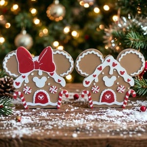 May include: Two gingerbread-style house decorations shaped like mouse ears. The left piece features a large red bow, while both have white icing details, red and white peppermint accents, candy cane trim, and a small mouse head icon on the door.