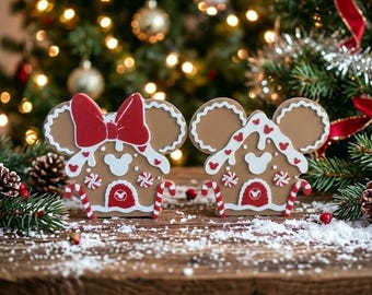 May include: Two gingerbread-style house decorations shaped like mouse ears. The left piece features a large red bow, while both have white icing details, red and white peppermint accents, candy cane trim, and a small mouse head icon on the door.