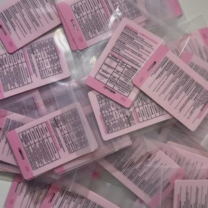 May include: A pile of pink and white cards in clear plastic sleeves. The cards contain text and diagrams related to neonatal care, with the words "NEONATAL COMPLICATIONS" and "VEAL CHOPS" visible.