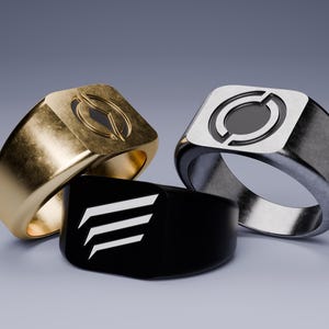 May include: Three signet rings in gold, silver, and black. The gold ring has a cutout design, the silver ring has a circular design, and the black ring features three white angled lines. Jewelry.