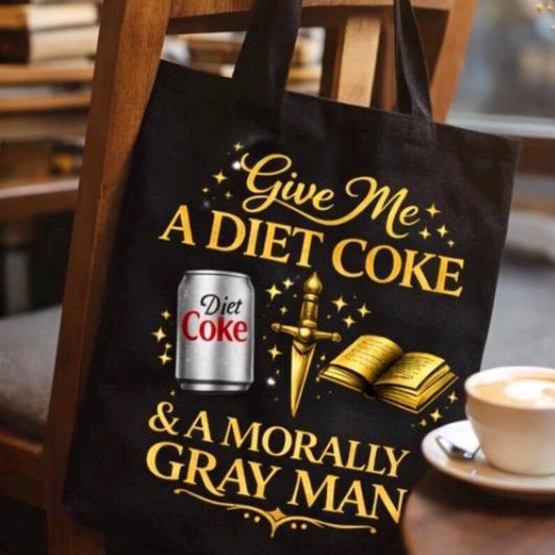 May include: Black tote bag with gold text that reads "Give Me A Diet Coke & A Morally Gray Man." The bag features a Diet Coke can, a sword, and an open book graphic.