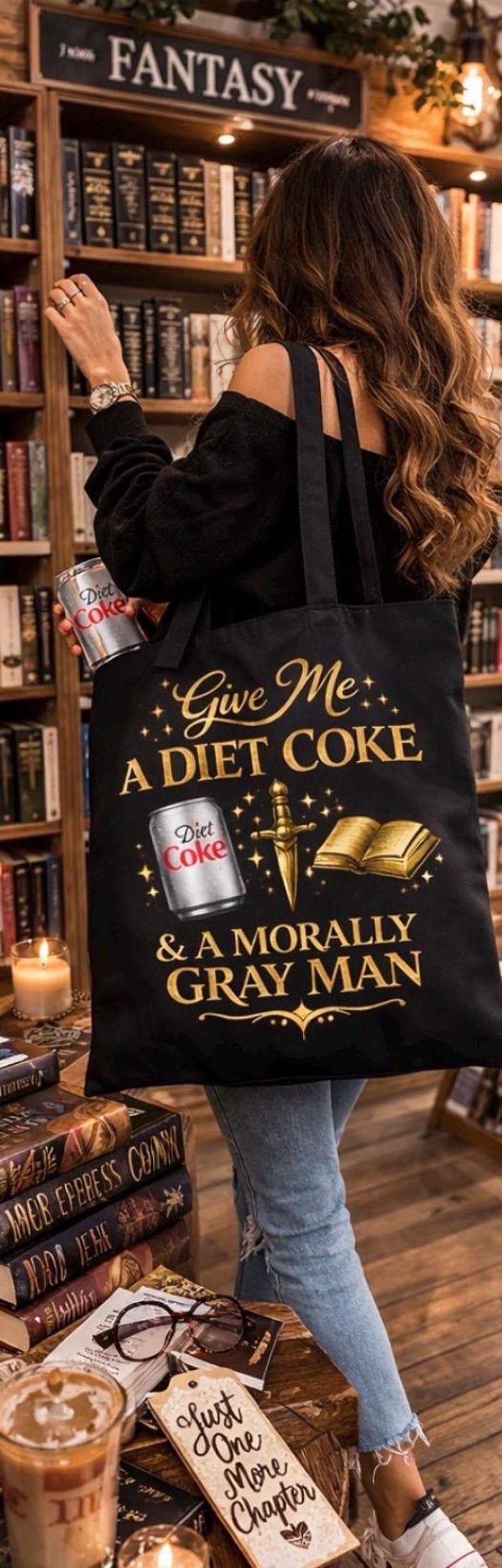 May include: Black tote bag with the text "Give Me A Diet Coke & A Morally Gray Man" in gold lettering. The design includes a Diet Coke can, a dagger, and a book. A Diet Coke can is held in the background.