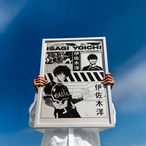 May include: A framed black and white print featuring manga-style illustrations. The print includes the name "ISAGI YOICHI" and Japanese text. The artwork depicts a character in a soccer uniform and other graphic elements against a blue sky.