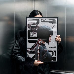 Op de afbeelding: Een ingelijste poster met een cyberpunk-thema. De poster toont een vrouw met kort zwart haar, een sigaret en een gedetailleerd ontwerp met de tekst "/CDPR.exe" en "REDENGINE 4". Het kleurenpalet is voornamelijk zwart, wit en rood.