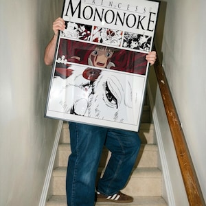 Może przedstawiać: Oprawiony plakat z grafiką z filmu animowanego "Księżniczka Mononoke". Plakat w czarnej ramie przedstawia kolaż obraz&oacute;w, w tym zbliżenie oka wilka i tytuł filmu.