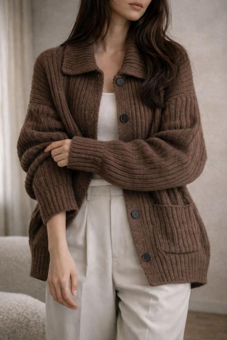 May include: A brown, button-down cardigan with a collared neckline and two front pockets. The ribbed knit sweater has large, dark buttons and a relaxed fit. The model is wearing a white tank top and light-colored pants.