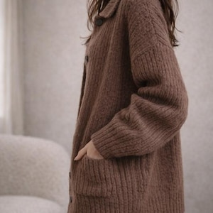 May include: A brown, button-down cardigan sweater with a collared neckline and two front pockets. The sweater is made of a thick, ribbed knit material. The model is wearing white pants.