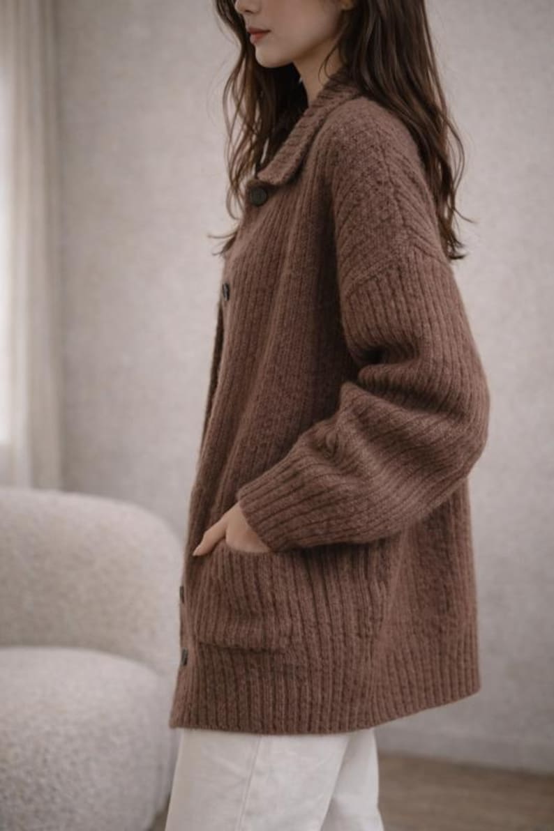 May include: A brown, button-down cardigan sweater with a collared neckline and two front pockets. The sweater is made of a thick, ribbed knit material. The model is wearing white pants.