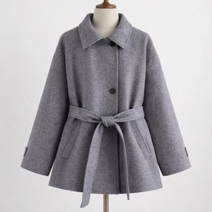 May include: A gray coat with a matching belt tied at the waist. The coat has a collar, two front pockets, and a single button closure. The sleeves are long, and the coat is displayed on a mannequin.