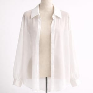 May include: A white, sheer button-down shirt with long sleeves and a classic collar, presented on a mannequin. The shirt is unbuttoned, showing the mannequin's shape. The fabric looks lightweight and flowing, suitable for warmer weather.
