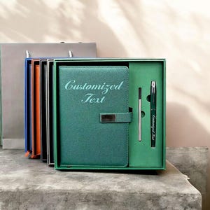 Könnte beinhalten: Ein tealfarbenes Notizbuch- und Stiftset mit dem Text "Customized Text" auf dem Notizbuchdeckel und dem Stift. Das Notizbuch hat einen silbernen Verschluss und befindet sich in einer grünen Box mit einem Stift und einer Nachfüllung.