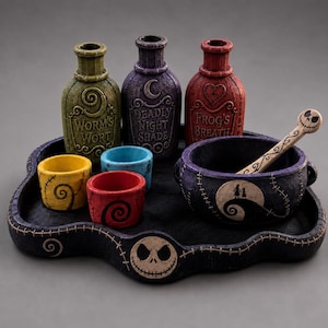 Op de afbeelding: Een decoratieve set bestaande uit een zwart dienblad met een schedelgezicht, drie flesjes met de labels Worm's Wort, Deadly Night Shade en Frog's Breath, drie kleine kleurrijke bekers en een donkere kom met een lepel met schedelhandvat.