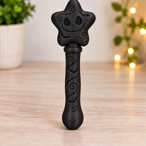 May include: A matte black wand featuring a star-shaped top with a carved skull face and small bat silhouettes. The handle is cylindrical with a spiraling vine pattern and additional bat motifs engraved along its length in a consistent dark finish.