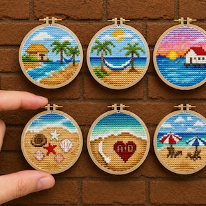 May include: Six circular wooden embroidery hoops containing cross-stitch art of beach scenes. Designs include a hut, palm trees with a hammock, a house over water, seashells, a heart with the letters A and D, and beach chairs with umbrellas.
